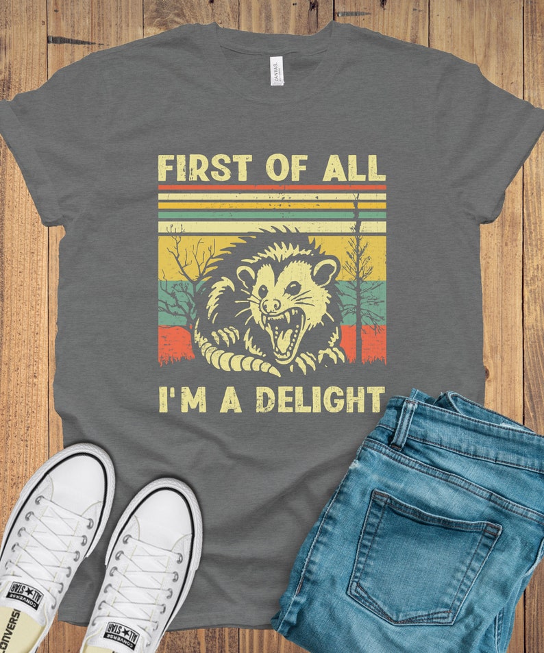 May include: A gray t-shirt with a vintage-style graphic of a possum with the text "First of all I'm a delight".