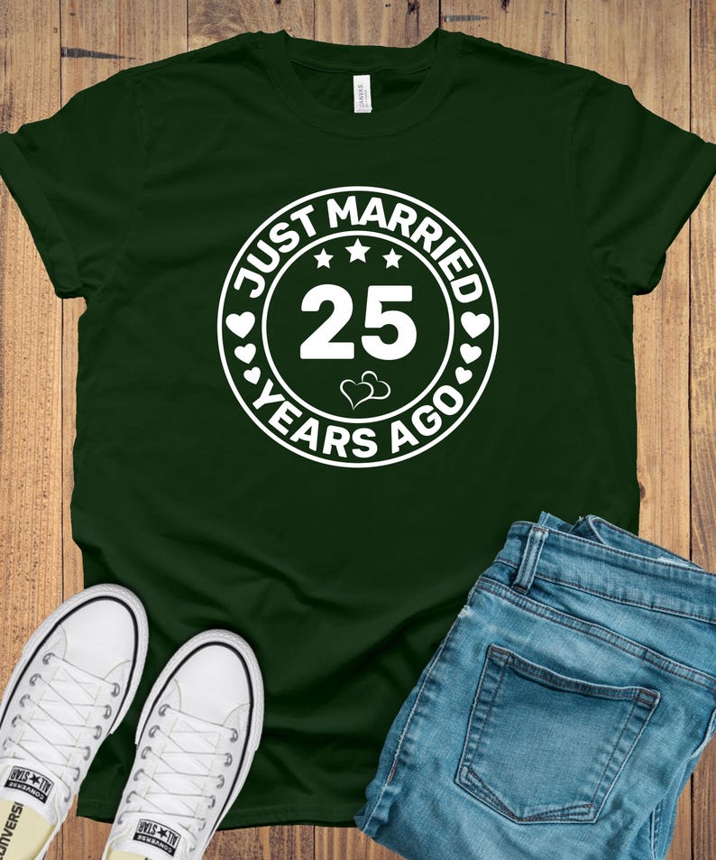 May include: Dark green t-shirt with a white circular graphic that reads "JUST MARRIED 25 YEARS AGO". The image also shows blue jeans and white canvas sneakers, suggesting a casual style.