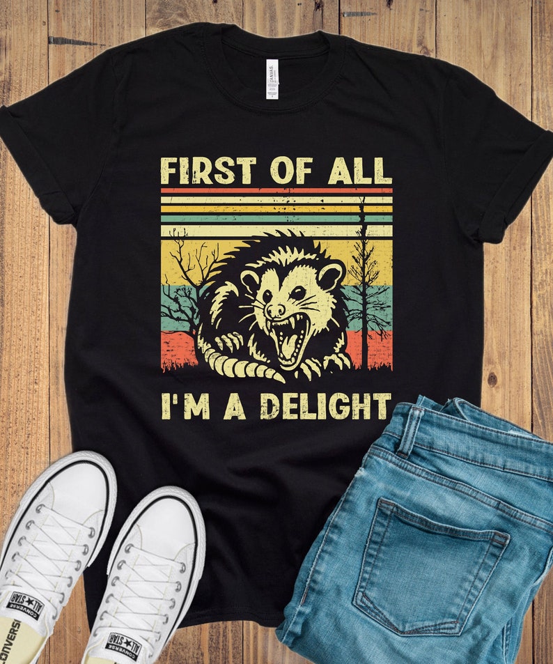 May include: Black t-shirt with a vintage-style graphic of a possum with the text "First of all I'm a delight".