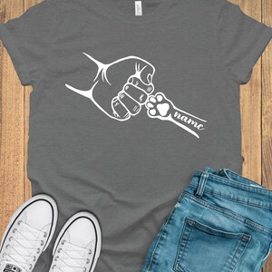 May include: A grey t-shirt with a white graphic of a human hand and a paw print holding pinky fingers. The text "name" is written below the paw print.