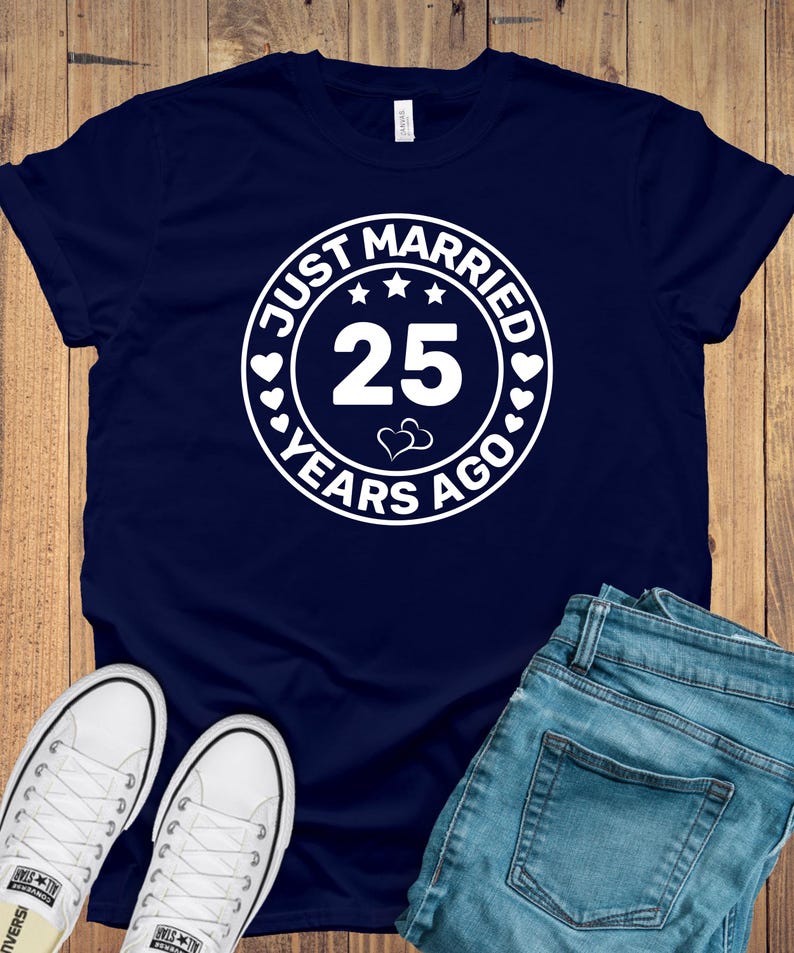 May include: Navy blue t-shirt with a white circular graphic that reads "JUST MARRIED 25 YEARS AGO" with stars and hearts. The image also shows white sneakers and blue jeans.