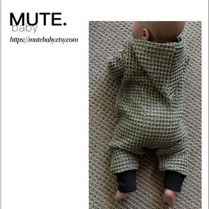 Könnte beinhalten: Ein Baby-Strampler mit Zipfelkapuze aus Waffelstoff wird gezeigt. Der Strampler ist olivgrün mit schwarzen Bündchen. Der Text auf dem Bild lautet "BABY ROMPER WITH PIXIE HOOD" und "MUTE. baby". Das Schnittmuster ist für die Größen 0m-6y.