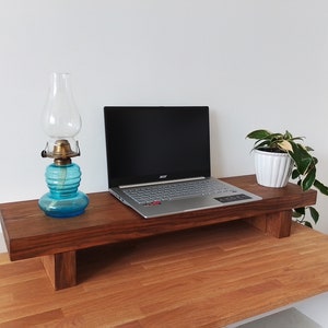 May include: A wooden laptop stand with a laptop, a blue glass oil lamp, and a potted plant. The stand is on a wooden desk.