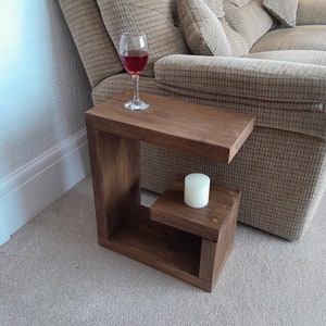 May include: A dark brown wooden side table with a shelf and a small top surface. A glass of red wine and a white candle are on the table.