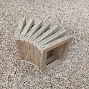 May include: A curved wooden bench made of multiple slats of wood. The bench is made of natural wood and has a rustic look.