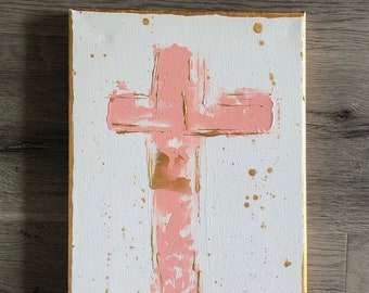 May include: A pink cross painted on a white canvas with gold accents and gold splatters.