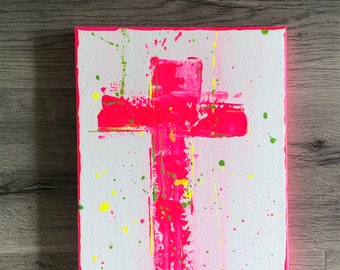 May include: A pink cross painted on a white canvas with yellow and green paint splatters.