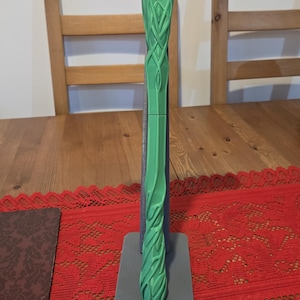 May include: A green 3D printed hammer with a detailed tree-like design on the handle. The hammer is displayed on a gray stand.