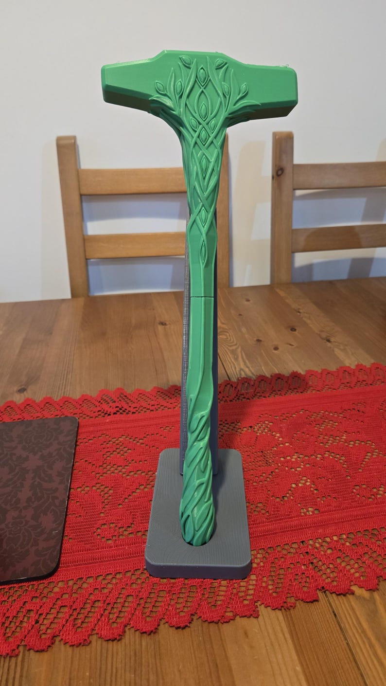 May include: A green 3D printed hammer with a detailed tree-like design on the handle. The hammer is displayed on a gray stand.