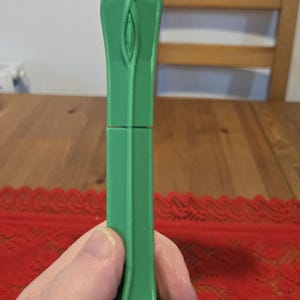 May include: A green plastic staff with a detailed design of intertwined vines and leaves. The staff is split in two pieces, showing the inside of the staff.
