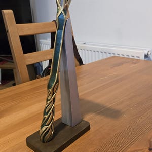 May include: A decorative hammer with a gold and green handle, featuring intricate details and colorful gems. The hammer is displayed on a wooden stand.