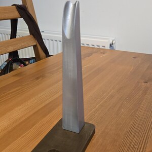 May include: A silver metal phone stand with a curved top and a dark brown wooden base.