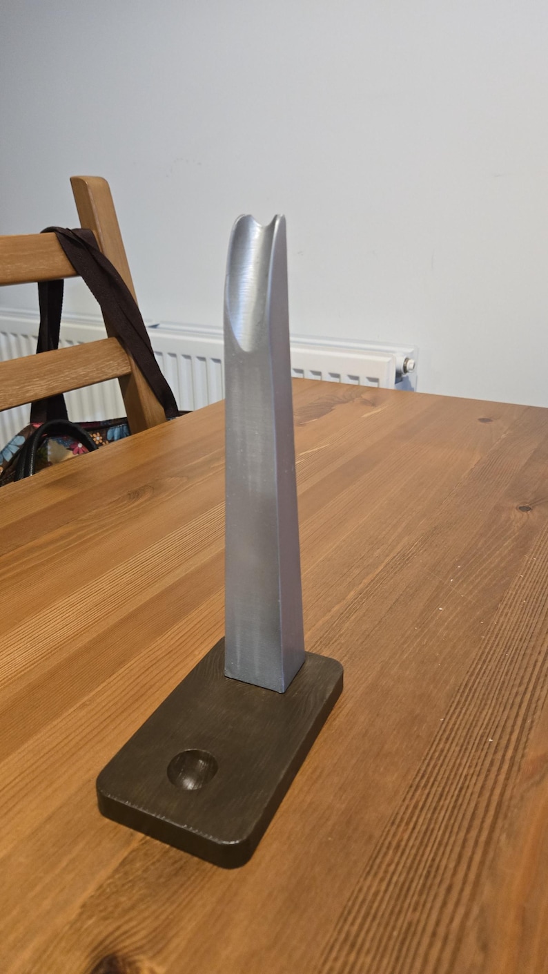 May include: A silver metal phone stand with a curved top and a dark brown wooden base.