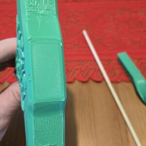 May include: A green 3D printed object with a rectangular panel on the side. The object has a textured surface and appears to be a part of a larger design.