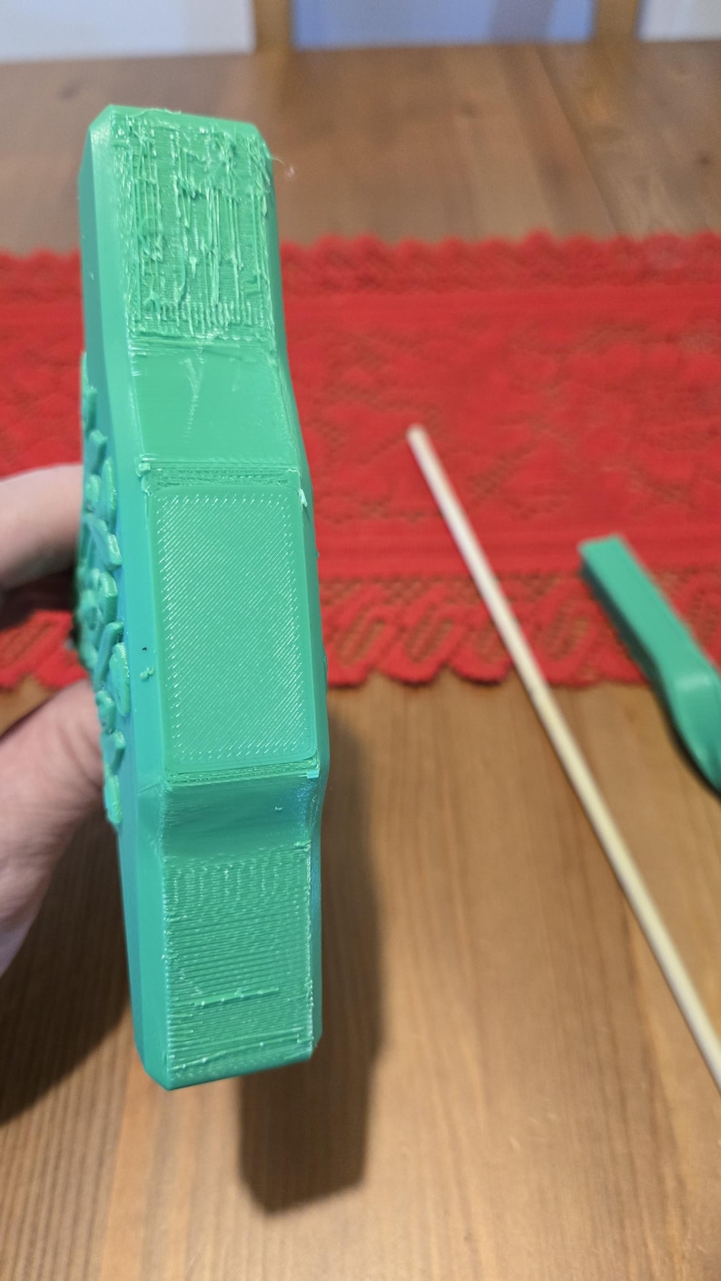 May include: A green 3D printed object with a rectangular panel on the side. The object has a textured surface and appears to be a part of a larger design.