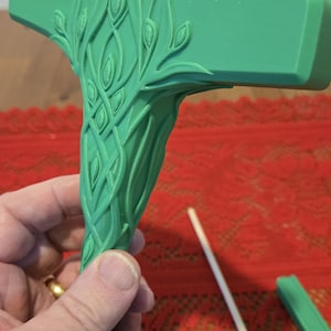 May include: A green 3D printed hammer with a detailed leafy design. The hammer has a curved handle and a flat head.