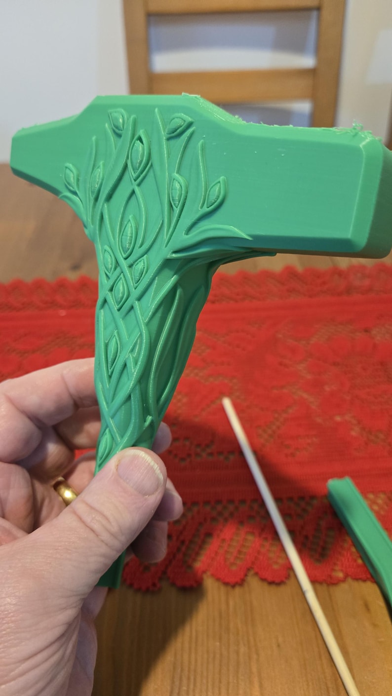 May include: A green 3D printed hammer with a detailed leafy design. The hammer has a curved handle and a flat head.