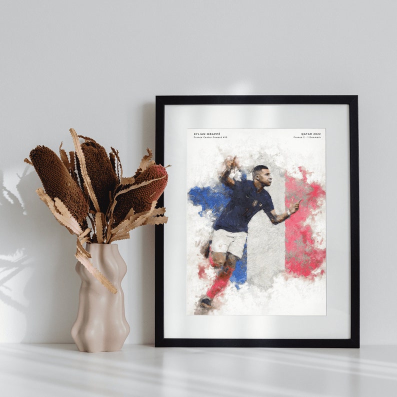 K&ouml;nnte beinhalten: Eine Aquarell-Illustration des Fu&szlig;ballspielers Kylian Mbapp&eacute; in Aktion, der ein blaues Trikot mit der Nummer 10 tr&auml;gt, vor dem Hintergrund der franz&ouml;sischen Flagge. Der Text "KYLIAN MBAPP&Eacute;" und "QATAR 2022" ist im Bild sichtbar.