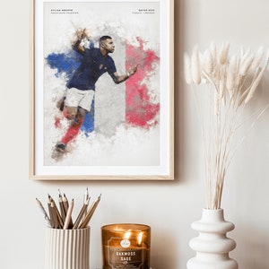 K&ouml;nnte beinhalten: Ein gerahmtes Poster mit einem Aquarellbild eines Fu&szlig;ballspielers in einem blauen Trikot mit der Nummer 10. Der Spieler rennt mit dem Ball vor einer franz&ouml;sischen Flagge. Das Poster enth&auml;lt den Text "KYLIAN MBAPPE" und "QATAR 2022".