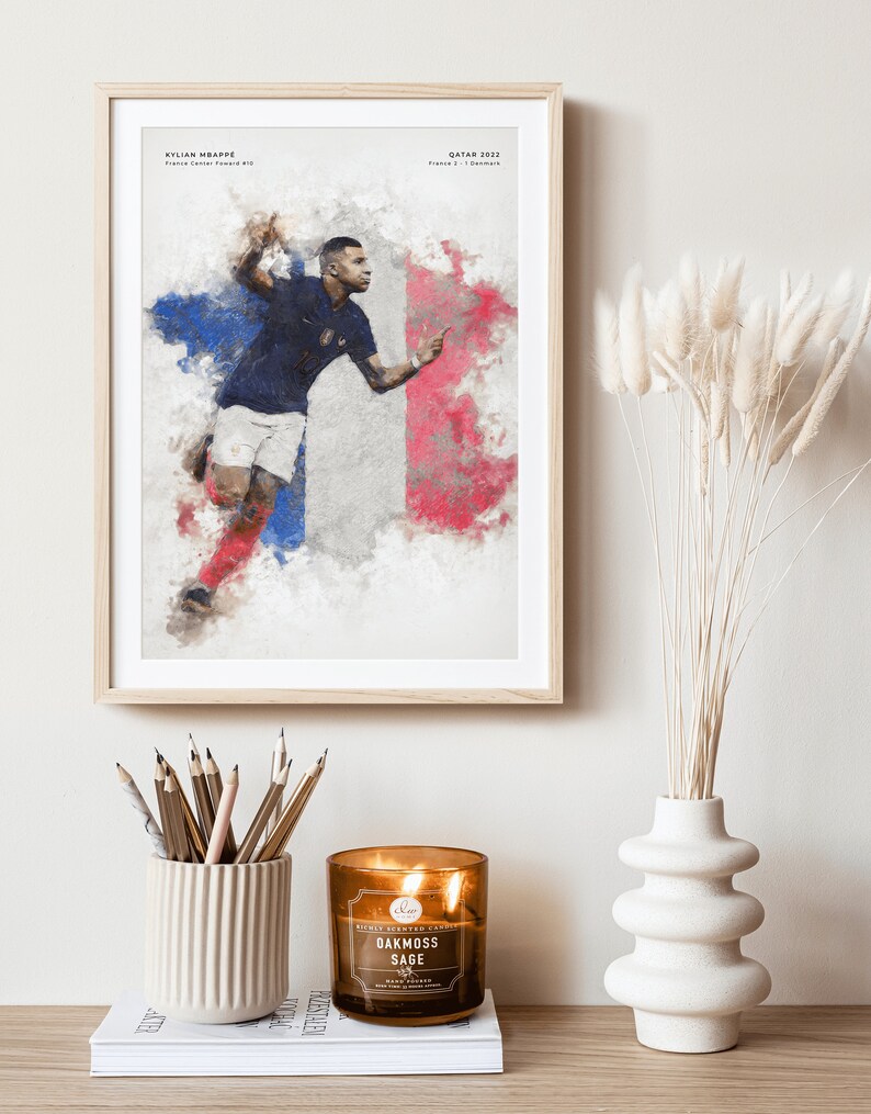 K&ouml;nnte beinhalten: Ein gerahmtes Poster mit einem Aquarellbild eines Fu&szlig;ballspielers in einem blauen Trikot mit der Nummer 10. Der Spieler rennt mit dem Ball vor einer franz&ouml;sischen Flagge. Das Poster enth&auml;lt den Text "KYLIAN MBAPPE" und "QATAR 2022".
