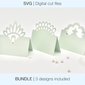 Op de afbeelding: Een set van drie afdrukbare plaatskaart sjablonen met verschillende decoratieve ontwerpen. De ontwerpen omvatten een pauwenveer, een bloemenpatroon en een wolkvorm. De plaatskaarten zijn lichtgroen van kleur en perfect om een ​​toets van elegantie toe te voegen aan elk evenement.