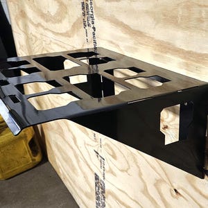 May include: Black metal wall-mounted shelf with multiple compartments, ideal for storing and organizing items. The shelf is mounted on a wooden surface.