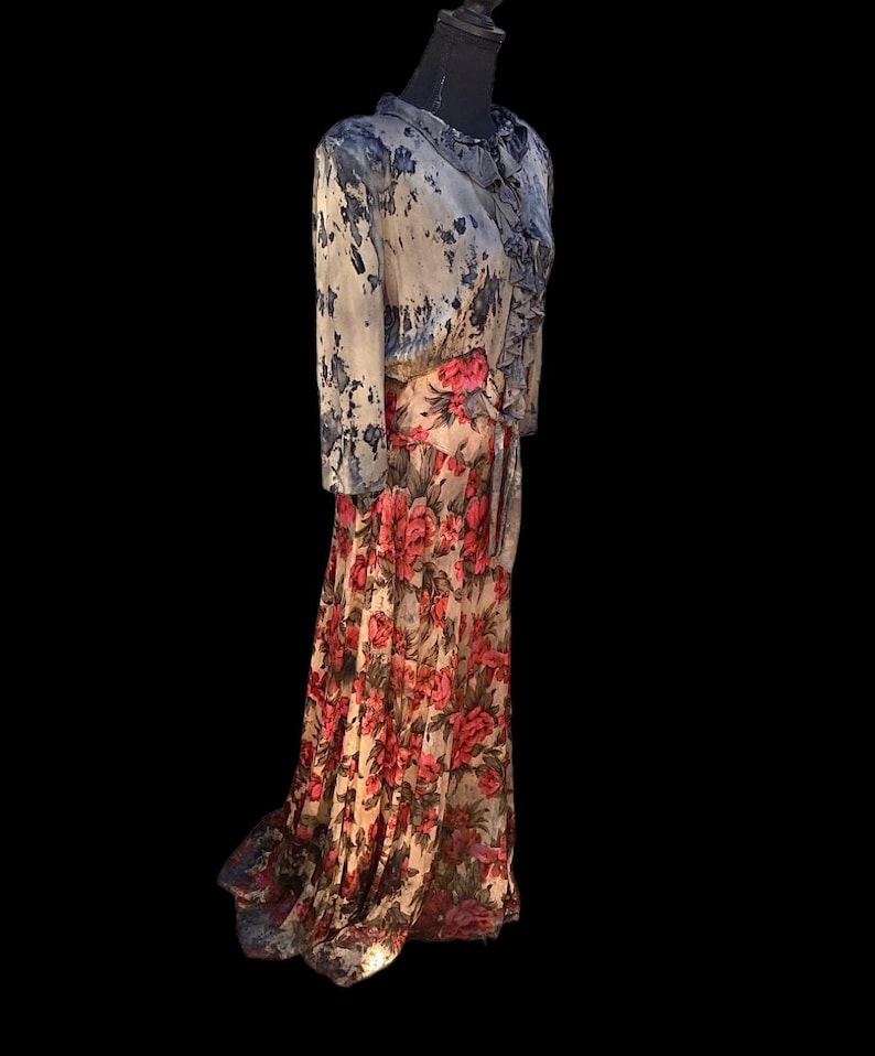 May include: A long, flowing dress with a floral pattern. The dress features a bodice with a blue and white watercolor design and a skirt with large red and pink flowers on a cream background. The dress has long sleeves and a ruffled collar.