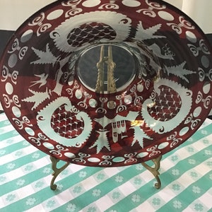 May include: A large, round, red glass bowl with a white etched design. The bowl is on a gold metal stand with three legs.