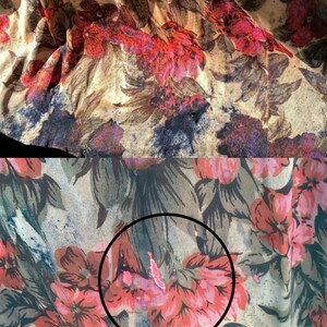 May include: Close-up of a fabric with a floral pattern. The design features large, stylized flowers in shades of red, pink, and purple against a beige background. The fabric has a slightly wrinkled texture, suggesting it may be a lightweight material.