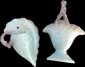 May include: Two vintage ceramic wall pocket planters in a light blue and white speckled glaze. One planter is shaped like a leaf with a twisted handle, the other is a basket-shaped planter with a handle.