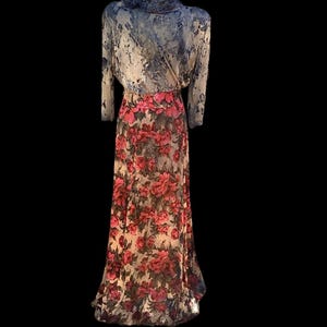 May include: A vintage floral print dress on a mannequin. The top is a light blue with a marbled pattern, and the long sleeves have a ruffled collar. The skirt is a cream color with a large red floral print.