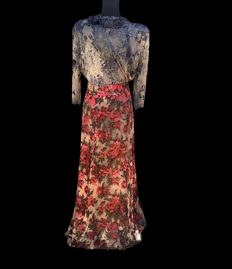 May include: A vintage floral print dress on a mannequin. The top is a light blue with a marbled pattern, and the long sleeves have a ruffled collar. The skirt is a cream color with a large red floral print.