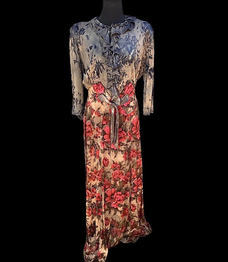 May include: A vintage floral print dress with a flowing silhouette. The dress features a high neckline with ruffles, long sleeves, and a tie waist. The skirt is adorned with large pink roses on a cream background.