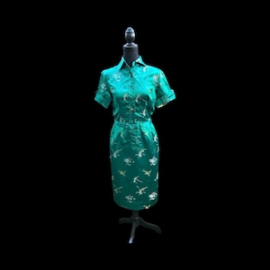 May include: A teal blue dress with a short sleeve button-up top and a matching skirt. The dress is decorated with a floral pattern in gold and white.