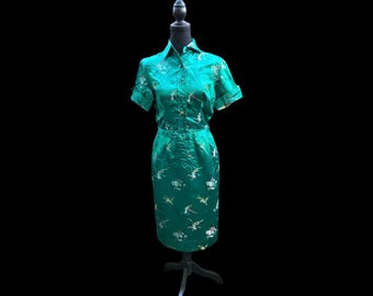 May include: A teal blue dress with a short sleeve button-up top and a matching skirt. The dress is decorated with a floral pattern in gold and white.