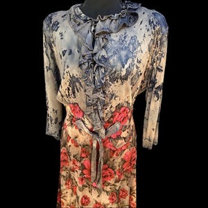 May include: A vintage-style dress with a unique design. The dress features a cream-colored base with a blue and gray abstract pattern on the top and sleeves. The lower portion showcases a floral print with red flowers. A gray tie belt cinches the waist.
