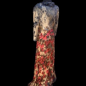 May include: A long, flowing dress with a floral print skirt and a patterned top. The top features a ruffled collar and long sleeves. The skirt is adorned with large, vibrant pink flowers against a cream background. The dress is displayed on a mannequin.