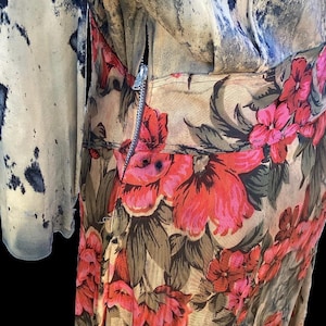 May include: A vintage floral dress with a zipper closure. The dress features a beige background with large red and pink flowers and green leaves. The sleeve on the left has a blue and beige pattern.