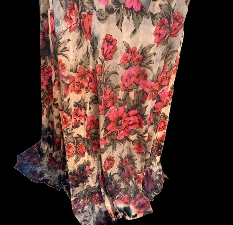 May include: A sheer fabric with a vibrant floral pattern. The design features large, red and pink roses with green leaves against a beige background. The fabric drapes, showcasing the floral print and a dark, watercolor-like border.