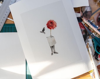 Peut inclure: Une impression d'art surréaliste représentant une fleur de dahlia rouge avec un oiseau en vol. La fleur est attachée à une silhouette avec des jambes et des chaussures. L'œuvre est sur papier blanc, entourée de fournitures d'art.