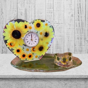 May include: A heart-shaped clock with a sunflower design and a clear glass tray with a smaller heart-shaped dish. The clock face is white with black numbers and hands.