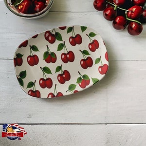 May include: White oval ceramic serving dish with a red cherry pattern. The dish is perfect for serving snacks or appetizers.