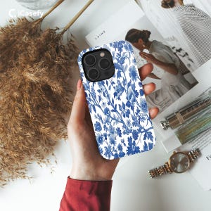 May include: A white phone case with a blue floral pattern. The case has a camera cutout and a raised lip around the edges.