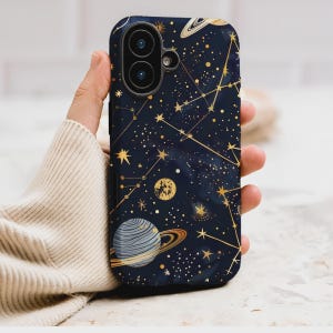 Könnte beinhalten: Eine marineblaue Handyhülle mit einem Himmelsdesign mit goldenen Sternen, Planeten und Sternbildern. Die Hülle hat eine glänzende Oberfläche und einen Kameraausschnitt. Das Design beinhaltet einen Planeten mit Ringen und einen Halbmond.