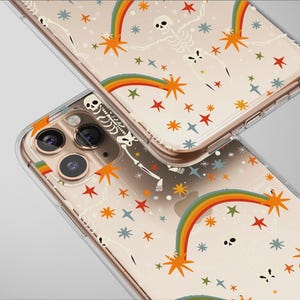 Op de afbeelding: Twee transparante telefoonhoesjes met een herhalend patroon van skeletten, regenbogen en sterren in oranje, rood, blauw en groen. De hoesjes hebben een goudkleurig frame en zijn licht gekanteld, waardoor het ontwerp wordt getoond.