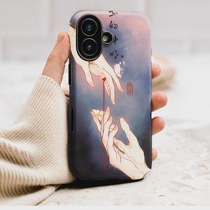 May include: A phone case featuring an artistic illustration of two hands reaching towards each other, connected by a red string. The design includes a flower and butterfly, with Chinese characters and a red seal. The case has a black border.