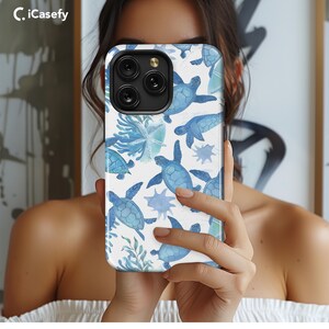 May include: A white phone case with a blue watercolor design of sea turtles and coral. The case has a black camera lens cutout and a clear iCasefy logo.