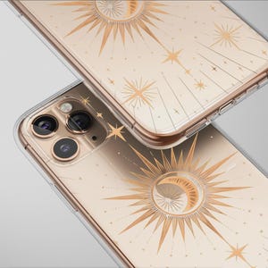 Może przedstawiać: Dwa przezroczyste etui na telefon z niebiańskim wzorem. Etui mają złoty wzór słońca, księżyca i gwiazd na beżowym tle. Etui są wykonane z przezroczystego materiału i mają złote obramowanie.