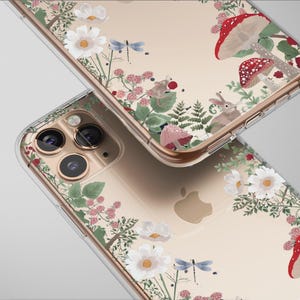 May include: Two clear phone cases with a floral and woodland design. The cases feature white flowers, red mushrooms, green leaves, and a dragonfly. A small rabbit is also visible in the design. The cases are on a light gray background.