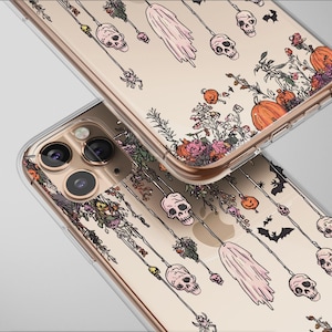 May include: Clear phone cases with a Halloween-themed design. The cases feature a repeating pattern of skulls, ghosts, bats, and pumpkins. Floral accents in orange, pink, and purple are also present. The cases are shown at an angle, with the camera lenses visible.
